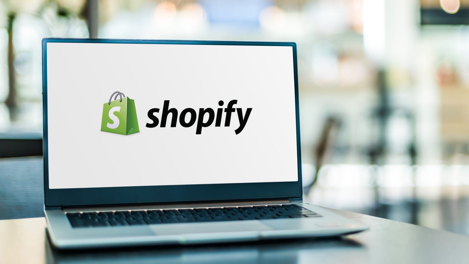 A laptop on a table displaying the Shopify logo on its screen, representing the discussion of top wholesale apps for enhancing Shopify store operations in 2024.